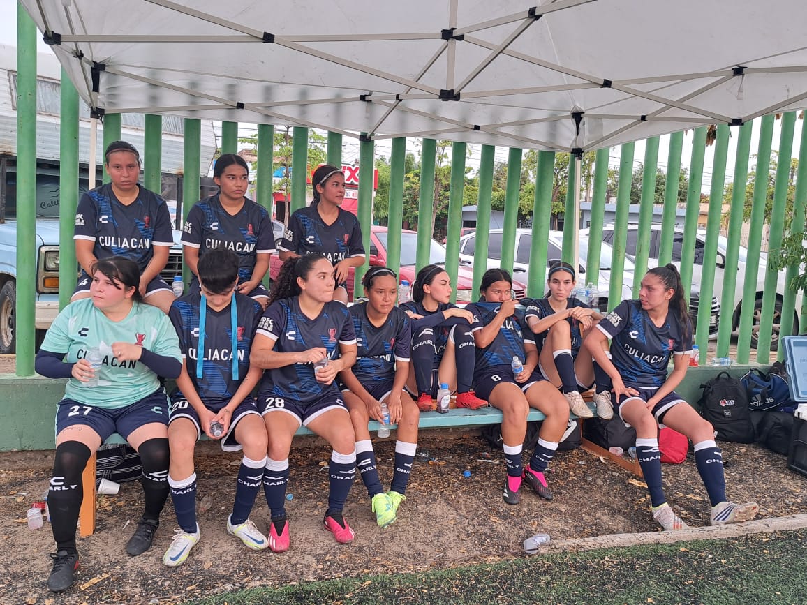 11 mujeres con ropa deportiva de un equipo de futbol sentadas en una banca