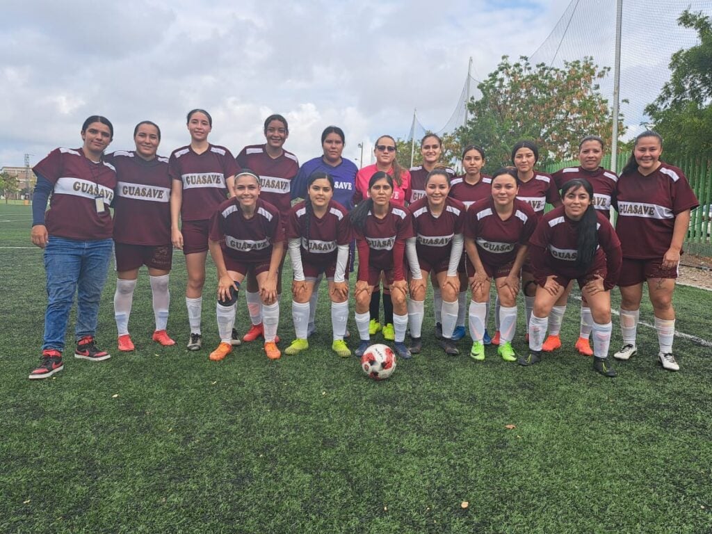 17 mujeres con ropa deportiva de un equipo de futbol en una cancha con césped y un balón posando para una foto
