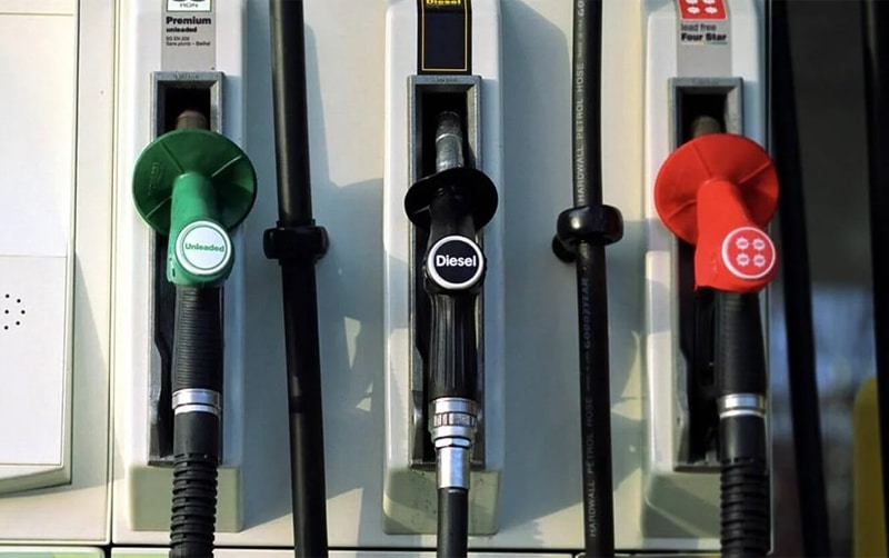 Bombilla de una estación de gasolina y 3 dispensadores de combustibles uno de color verde, otro negro y otro rojo