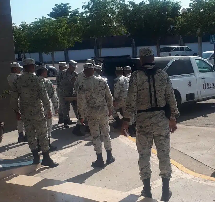 Personas paradas con uniforme de la Guardia Nacional y al fondo una carroza estacionada con la cajuela abierta