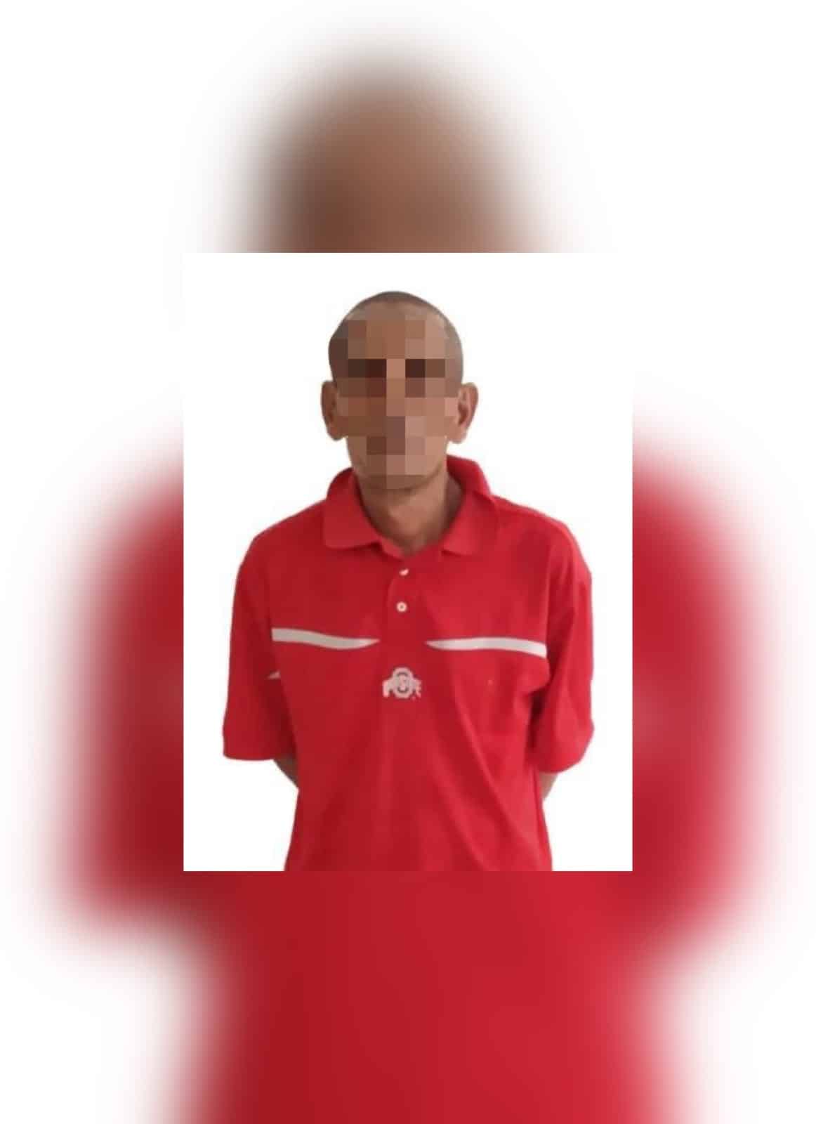 Una persona sin cabello con playera roja y la cara tapada