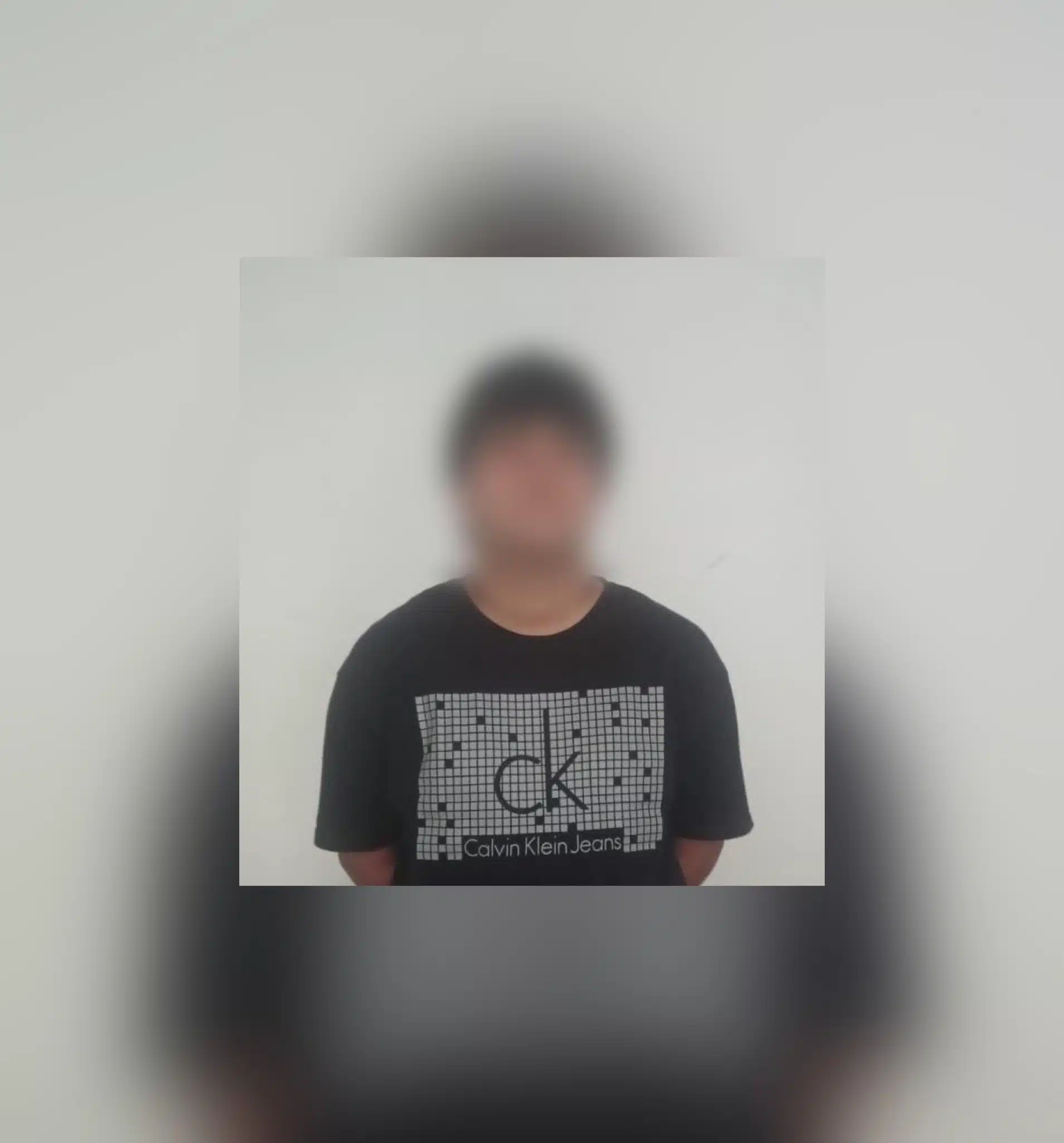 Hombre detenido con playera negra y letras blancas, y la cara tapada