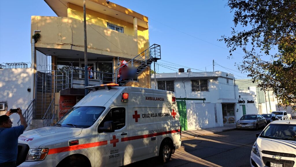 2 personas en las escaleras, una de ellas tapando a otra, un poste, casas, una ambulancia y carros