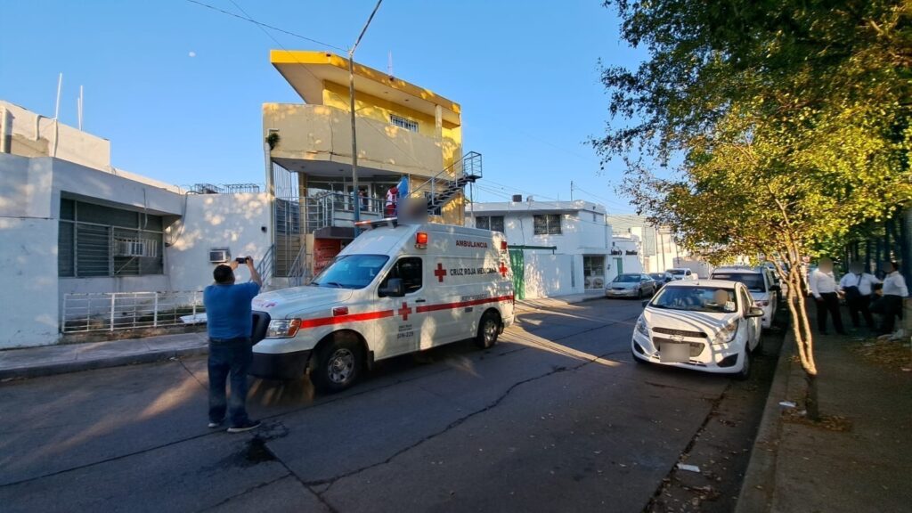 2 personas en las escaleras, una de ellas tapando a otra, un poste, casas, una ambulancia. carros y personas