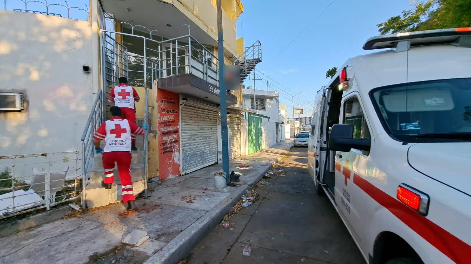 2 personas subiendo unas escaleras, un poste, una casa de 2 pisos, una parte de la ambulancia y un carro al fondo