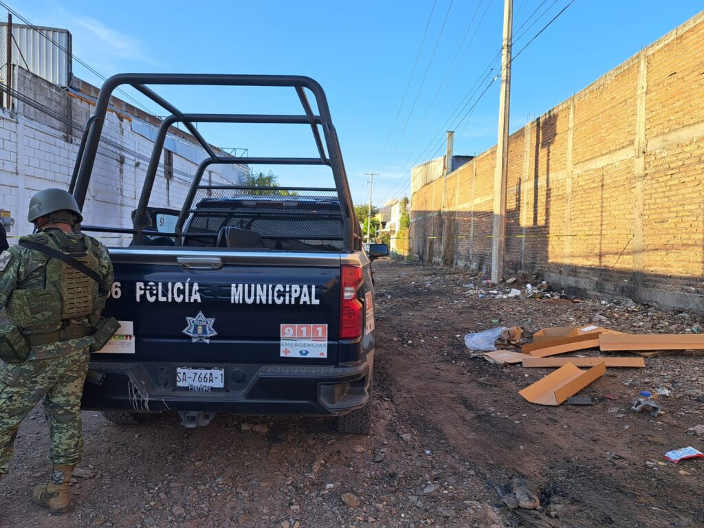 Camioneta de la policía parada sobre una calle de terracería y una persona atrás de ella, paredes de construcciones