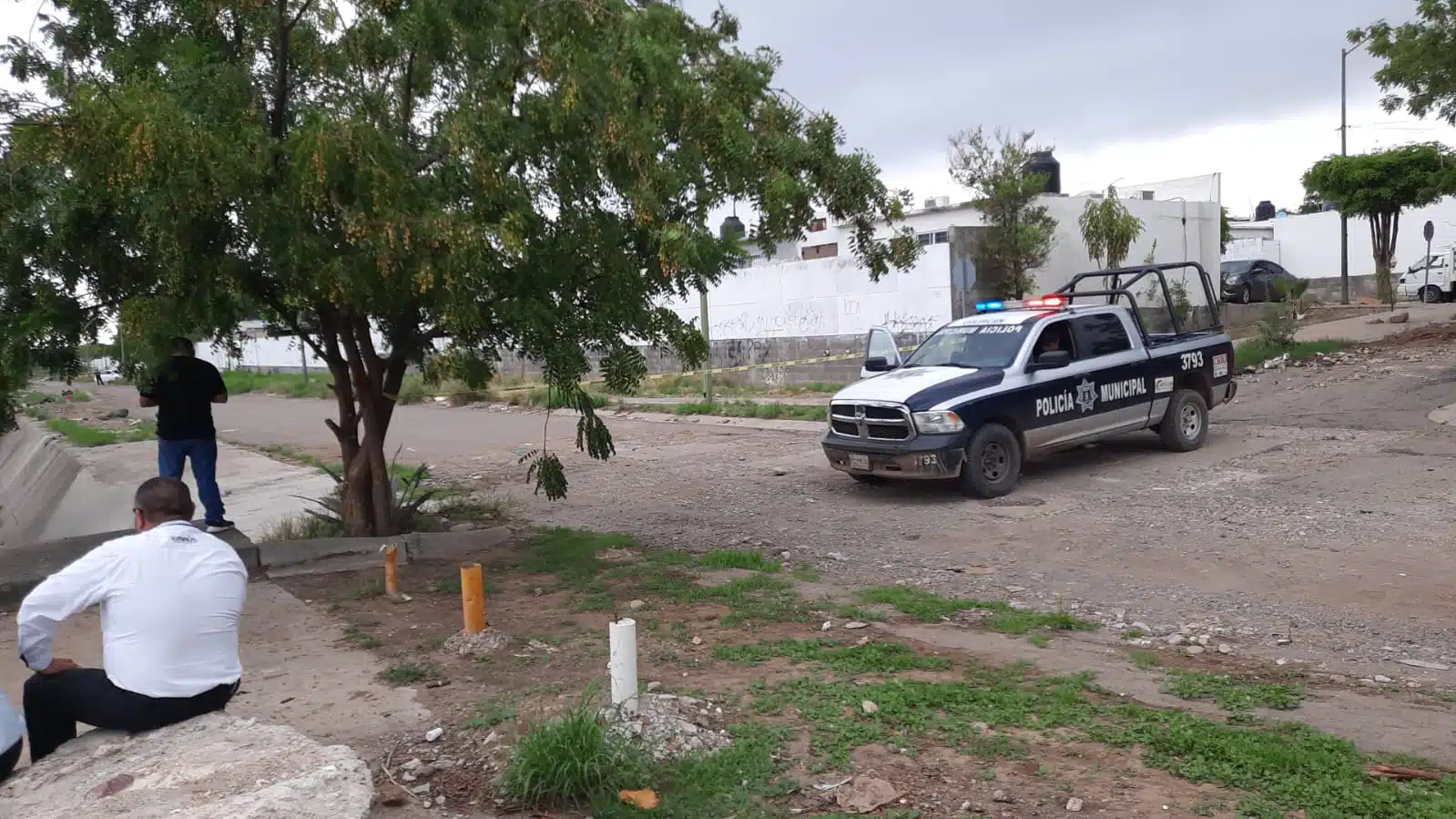 Una camioneta de la policía Municipal de Culiacán, árboles, calle, casas y 2 personas