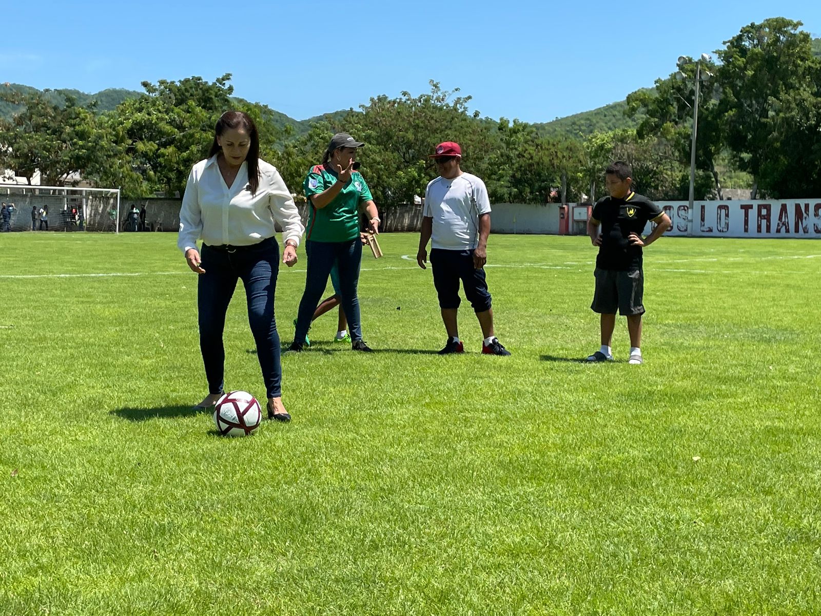 Una persona perfilándose para patear una pelota de futbol en una cancha y 3 más al fondo