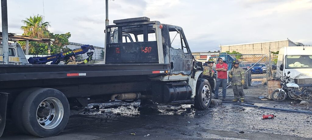 Un camión tipo grúa quemado, una persona al lado y otras 3 enfrente