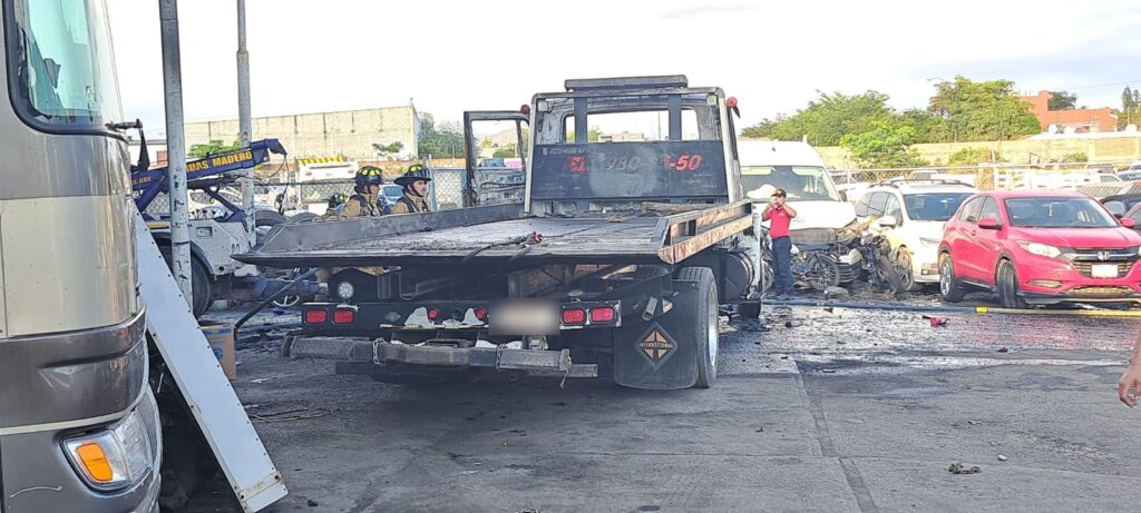 Un camión tipo grúa quemado y dos personas al lado, y carros al fondo