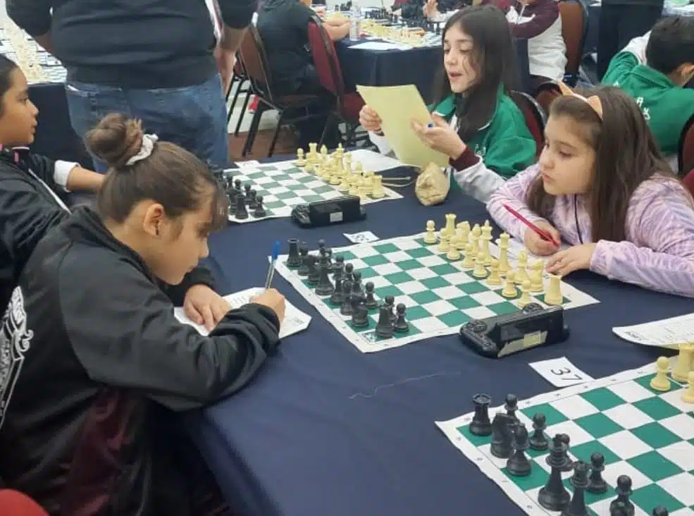 Niñas frente a un tablero de ajedrez; están jugando