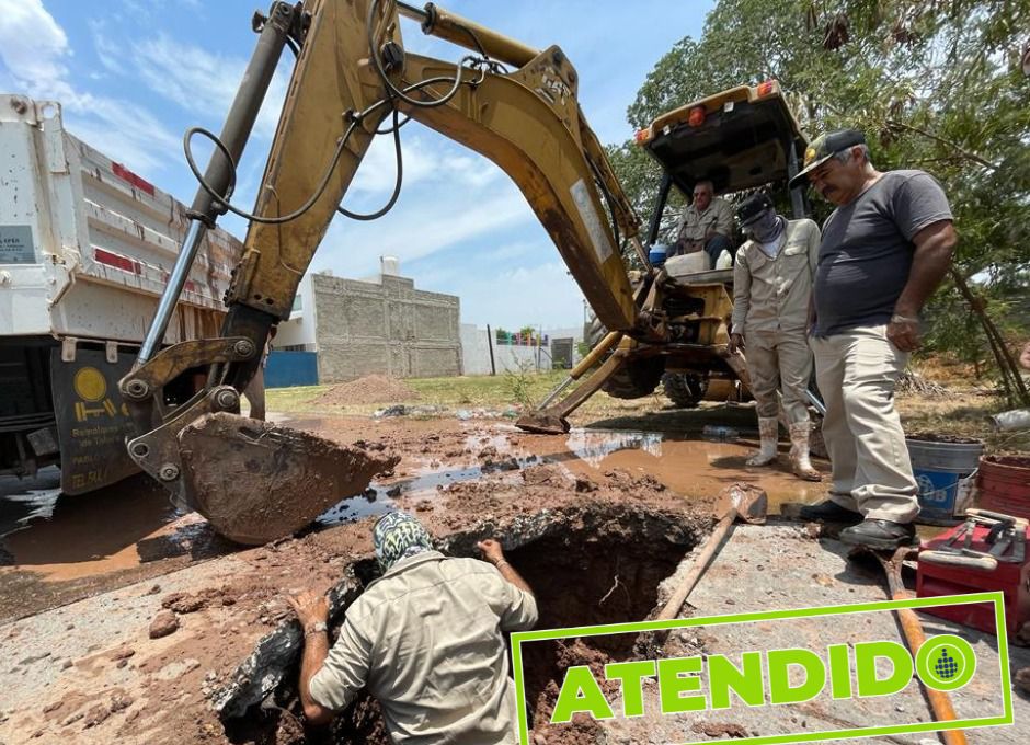 Una retoexcavadora, la parte trasera de un torton, una persona adentro de un socavón y dos personas mirándolo, al fondo arboles y paredes de casas, un recuadro color verde con letras en la esquina inferior