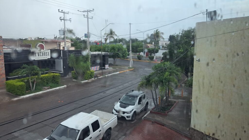 Calle, carros y casas mojadas por la llovizna y cielo nublado