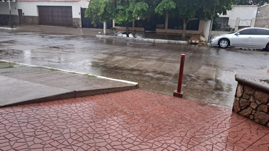 Gotas de agua cayendo al pavimento, la calle mojada, casas y un carro estacionado en la calle