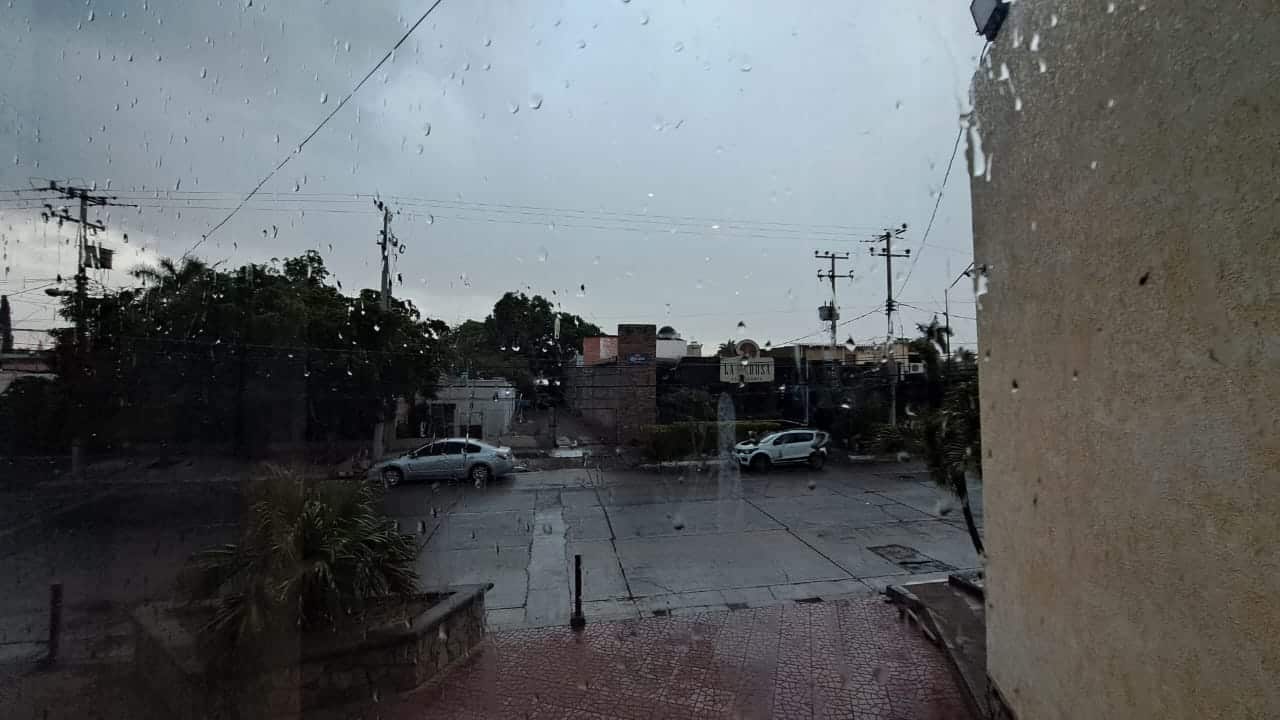 Cristal con gotas de agua, calle mojada, casas y dos carros estacionados en la calle