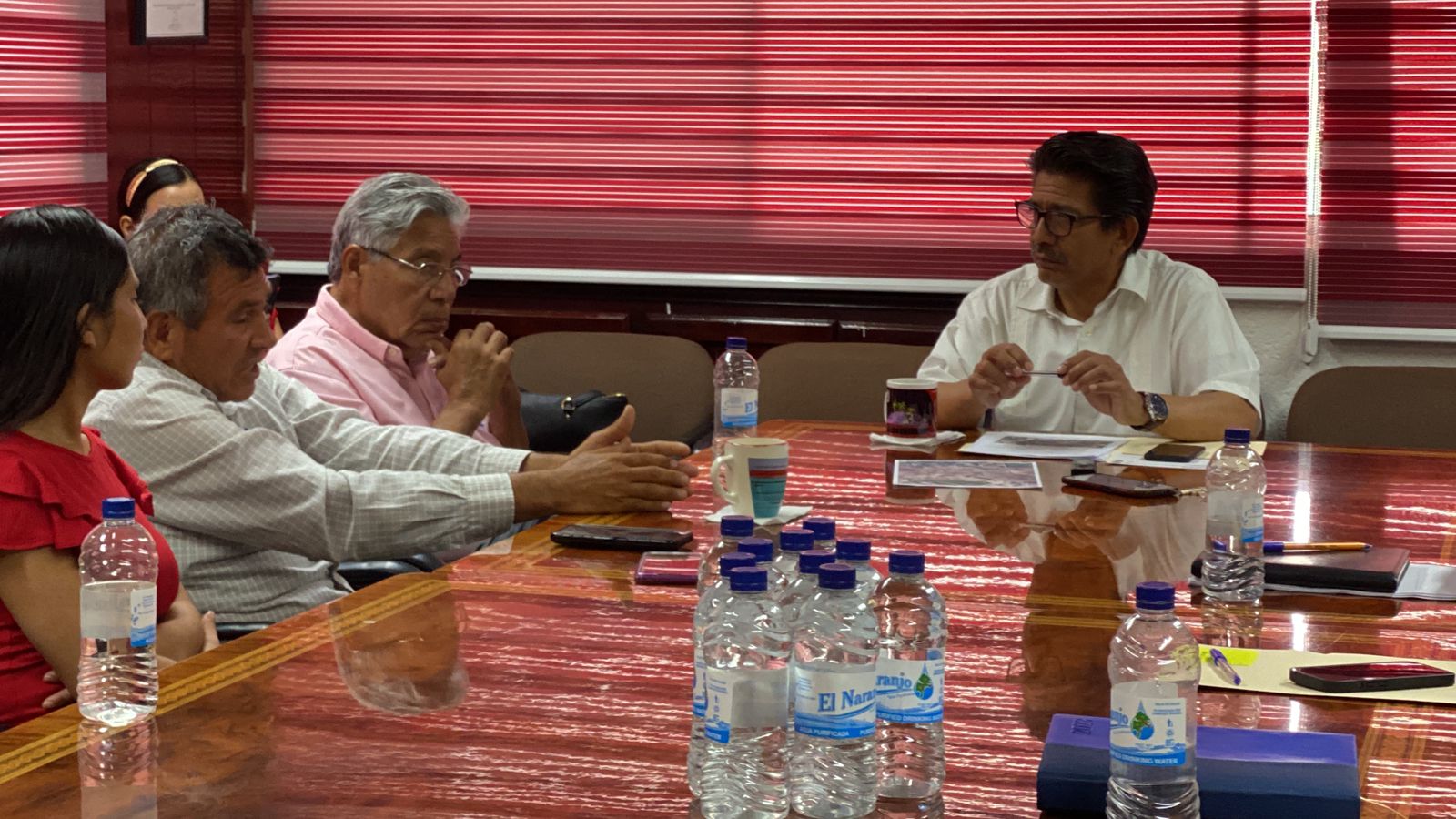 Personas sentadas reunidas, una mesa larga, botellas de agua y tazas