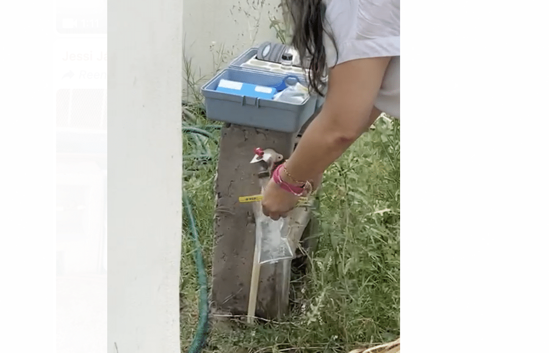 Llave del agua abierta, manos de una persona con una bolsita llenándola del líquido, pasto y una estructura de concreto