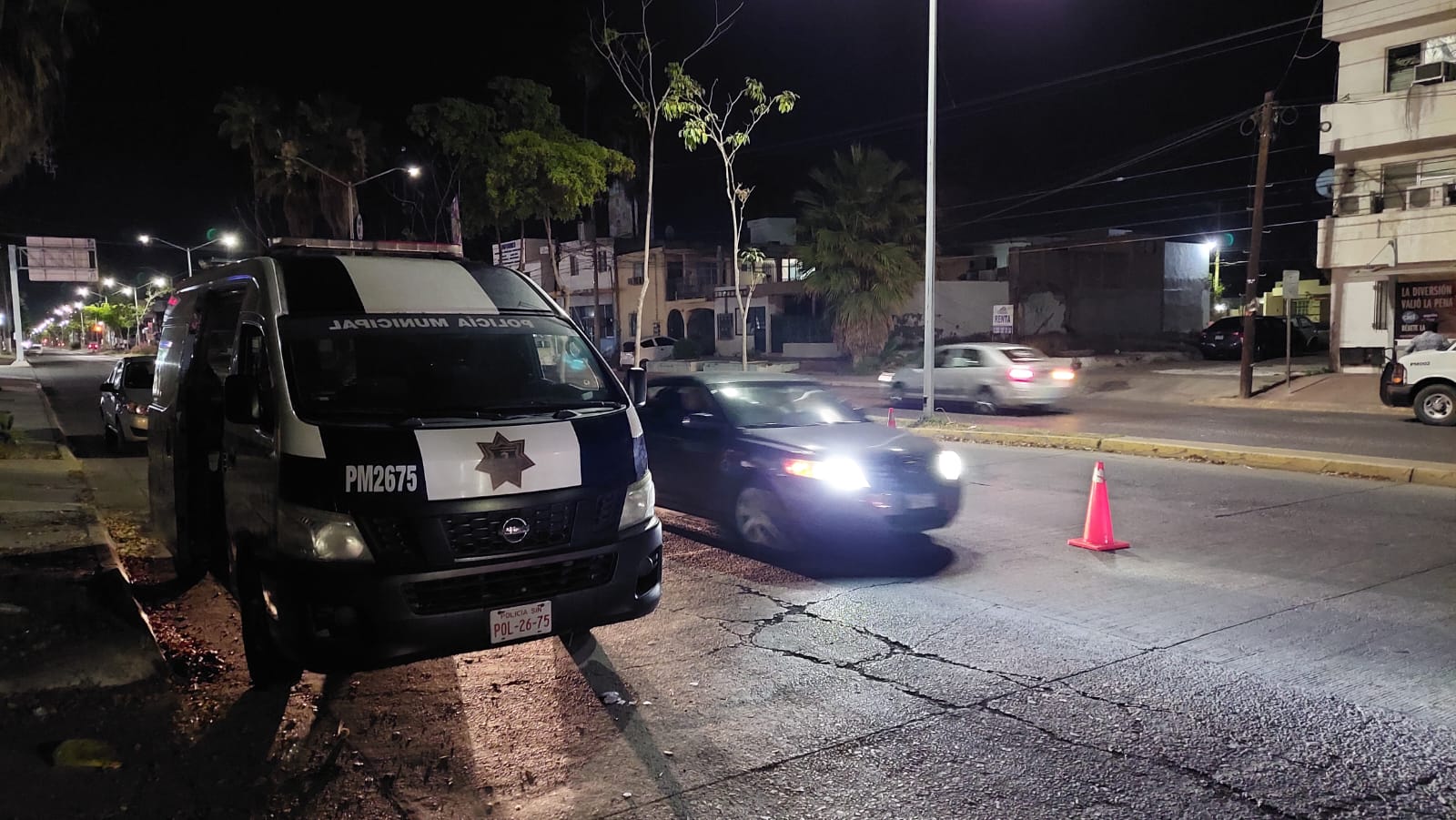 Una vagoneta, un carro, bulevar pavimentado, árboles, postes y cono color anaranjado