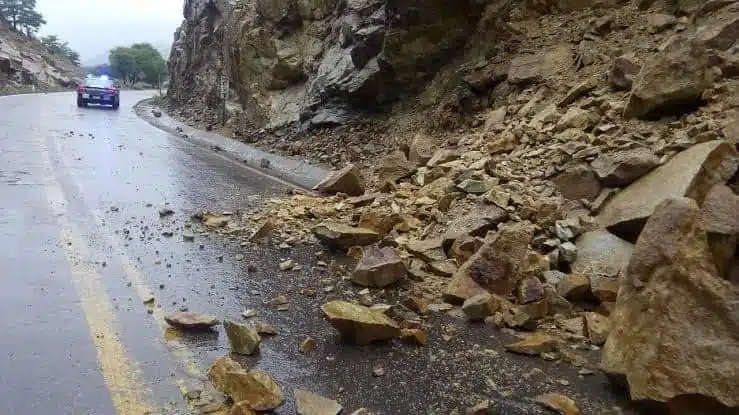 Piedras en la carretera, asfalto mojado y una patrulla al fondo