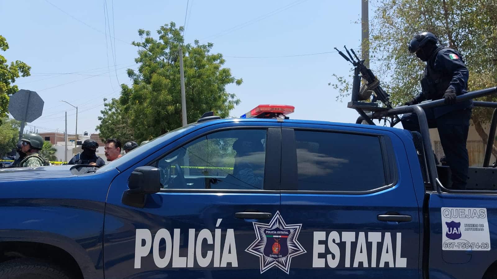 Camioneta de la Policía Estatal con una persona en la parte trasera con un arma, otra en el asiento del piloto y 3 personas más a un lado de ella