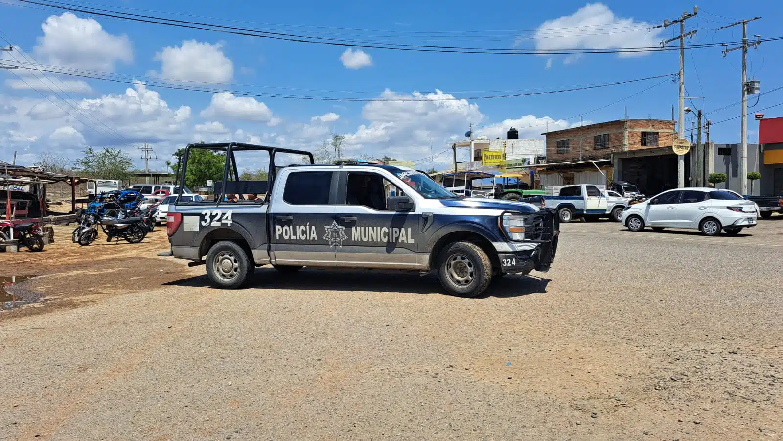 Camioneta de la Policía Municipal parada sobre la calle, carros y casas al fondo