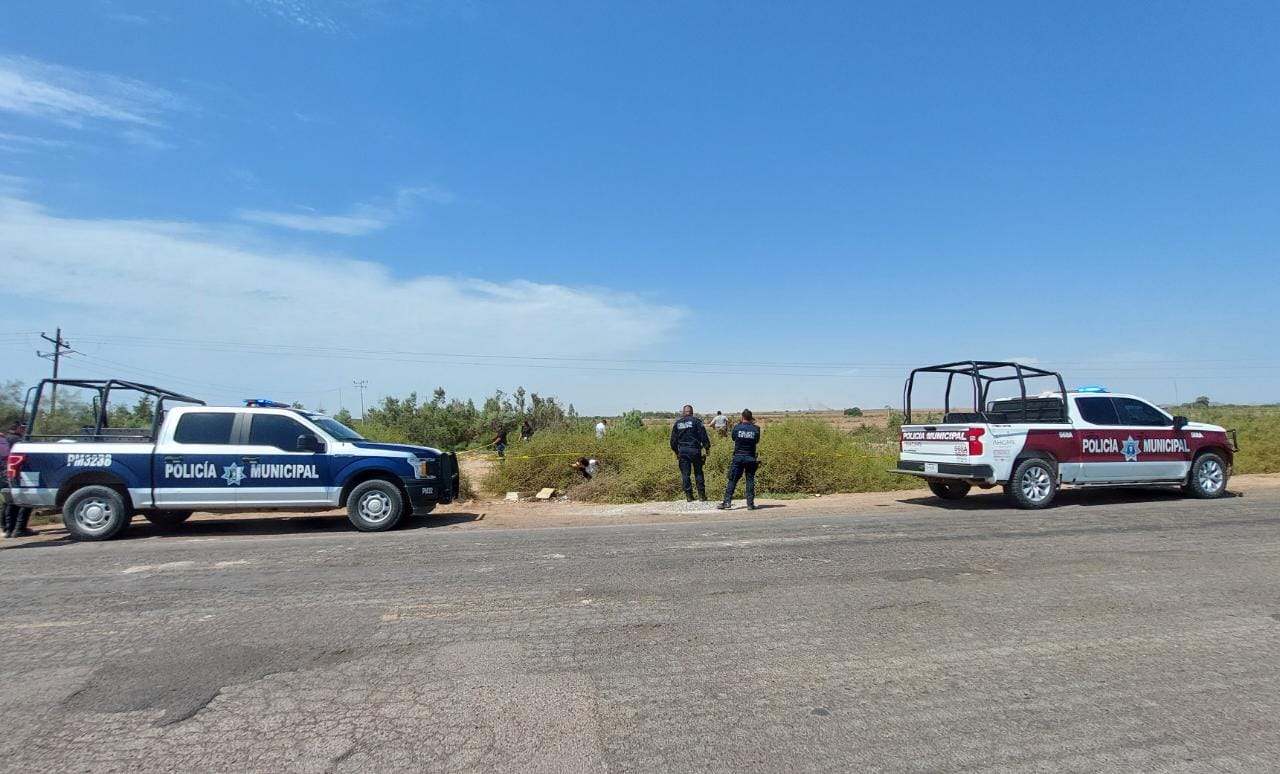 Dos camionetas de la policía estacionadas a un costado de la carretera, dos personas mirando hacia un canal