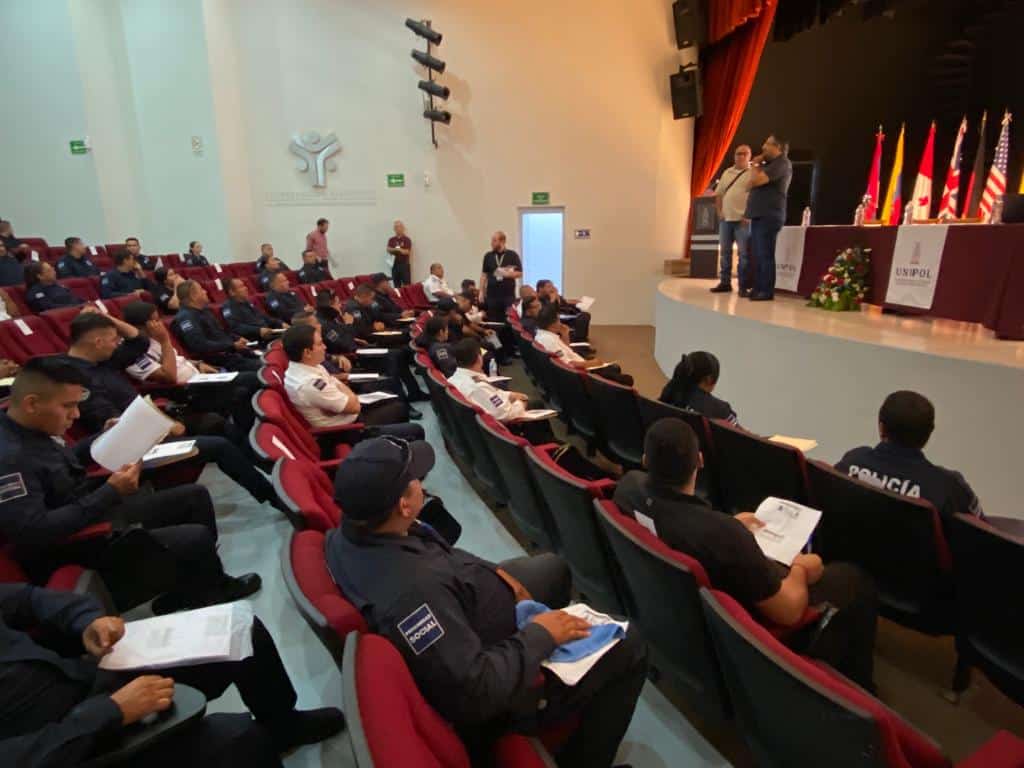Personas sentadas en un auditorio, una mesa, banderas y paredes