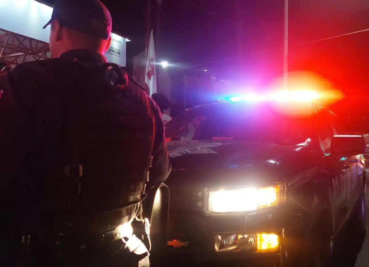 Una persona de espaldas y al fondo una camioneta de policía con las torretas y las luces prendidas