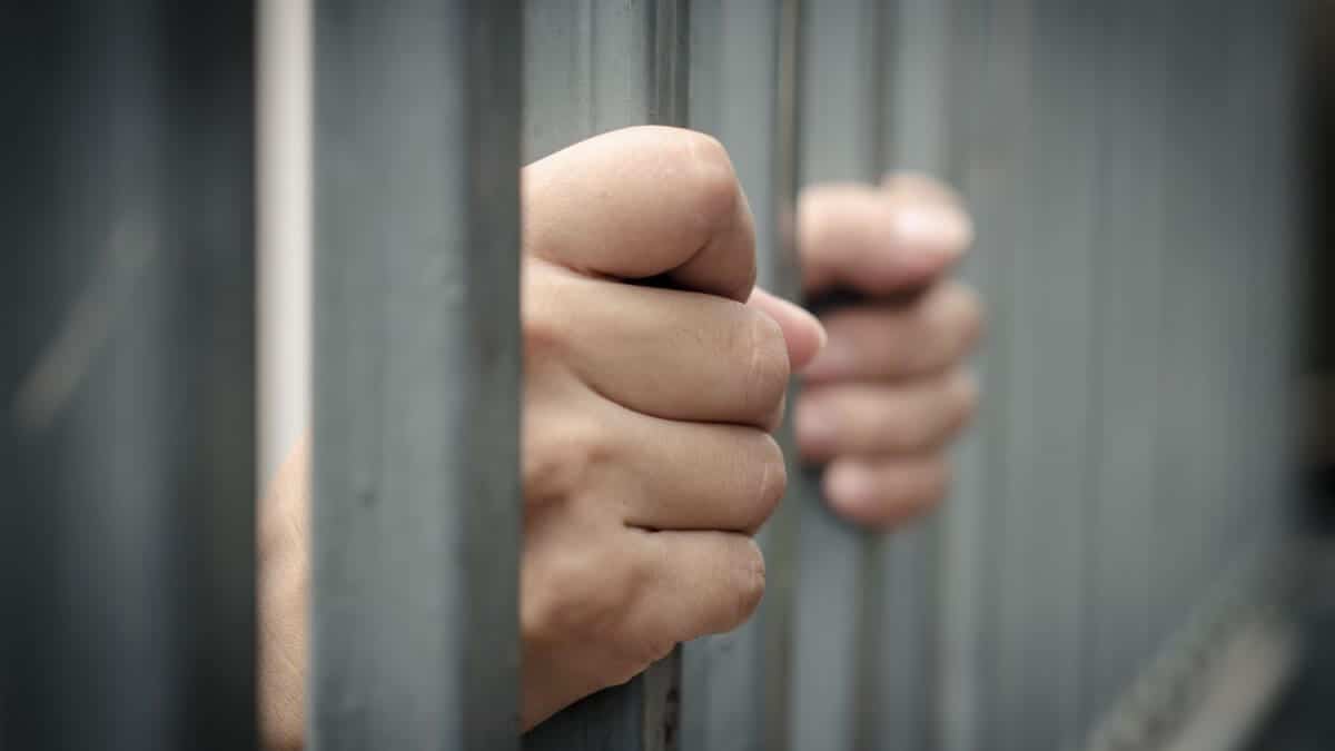 Manos de una persona agarrando los barrotes de una celda de prisión
