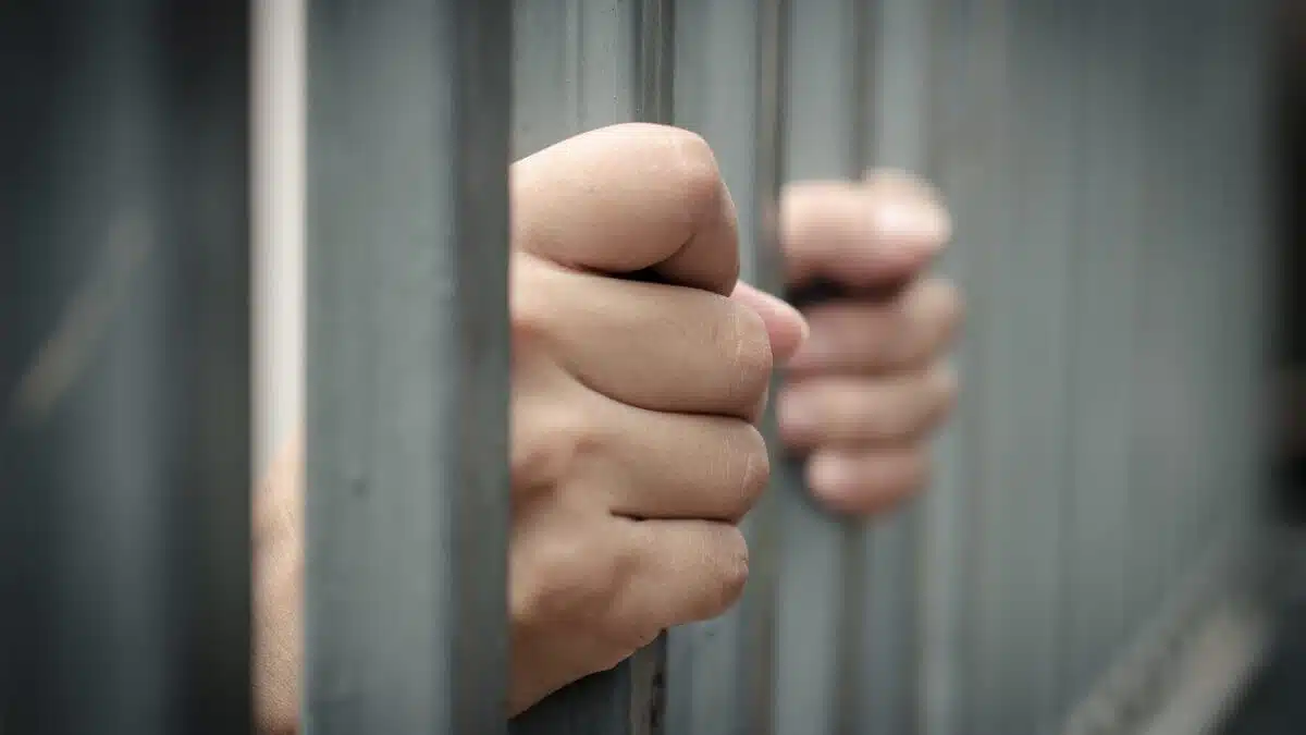 Manos de una persona agarrando los barrotes de una celda de prisión