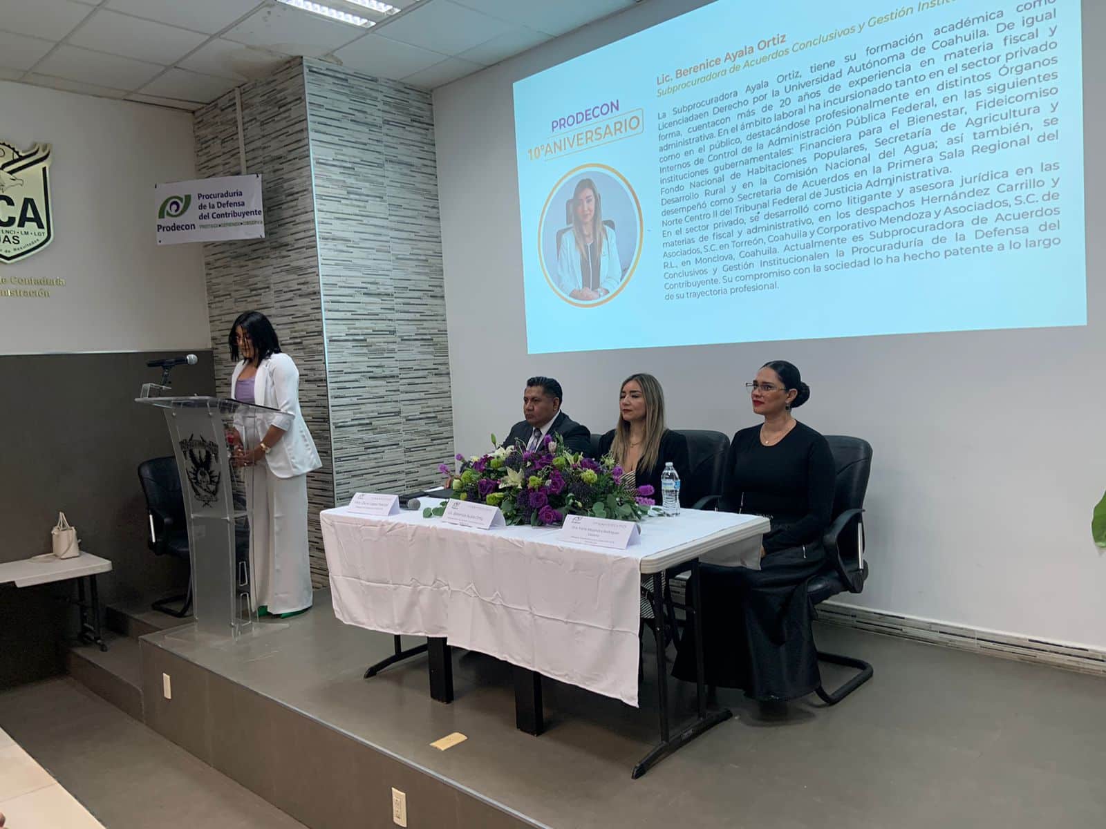 Tres personas sentadas tras una mesa y una persona más en el pódium