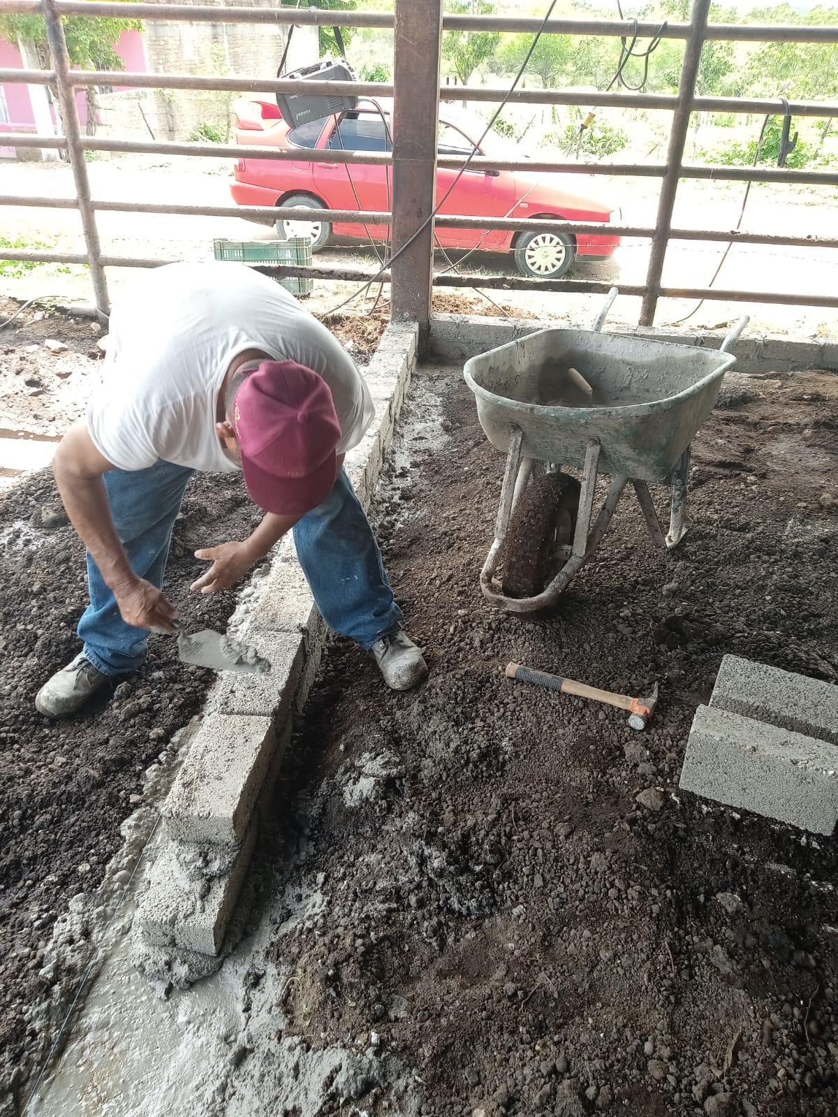 Una persona con gorra trabajando, bloques, carrucha, martillo, jaba y un carro al fondo