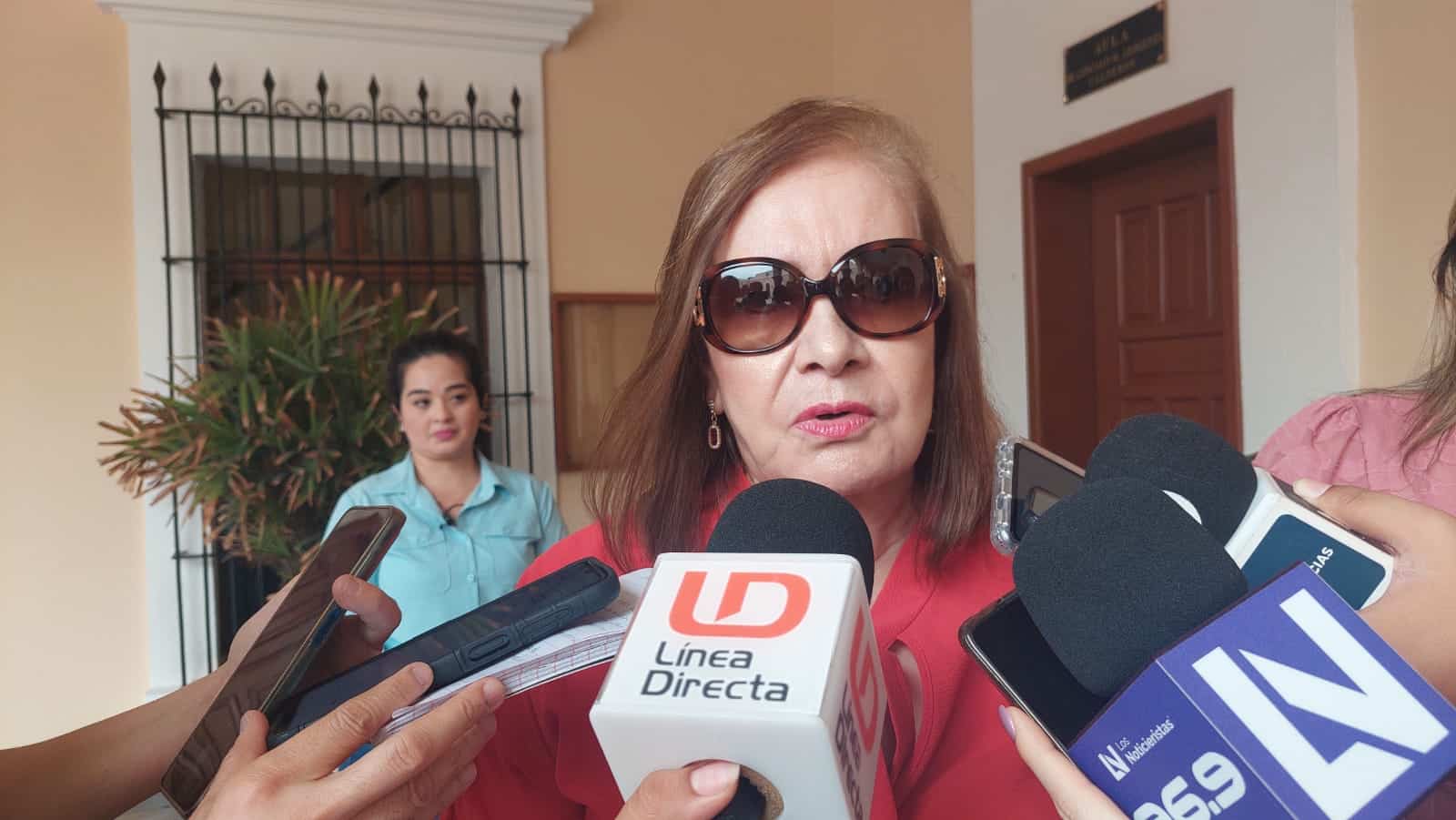 Una persona con lentes y varios micrófonos de medios de comunicación