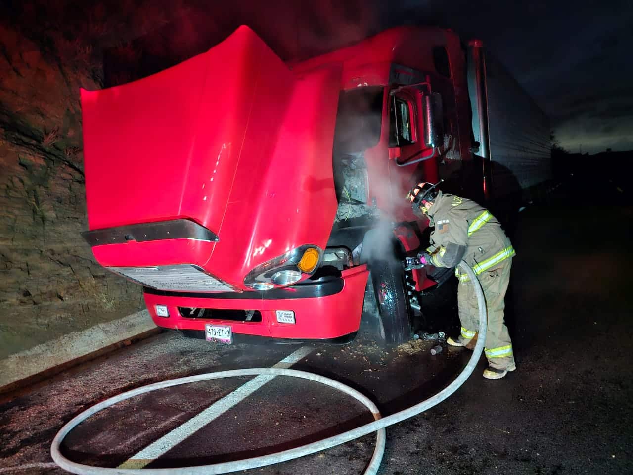 Tráiler con el cofre estacionado en la carretera y una persona con una manguera echándole agua