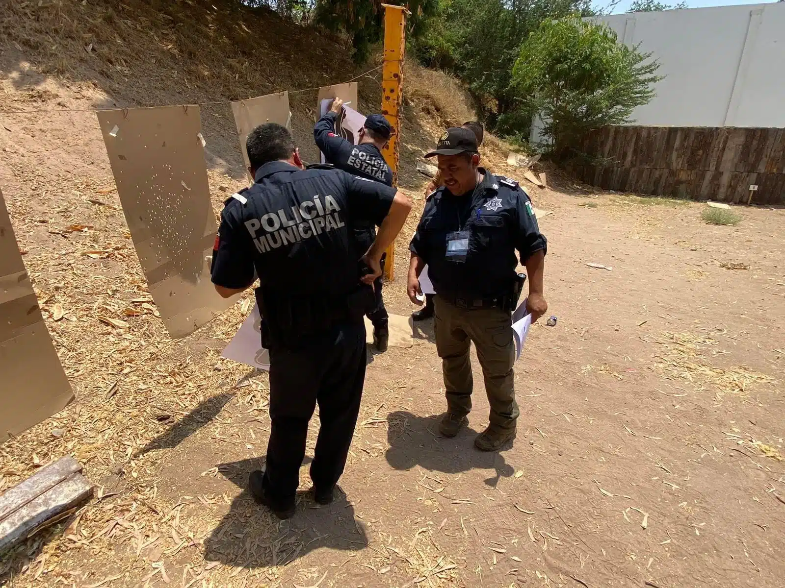 3 personas con uniforme de policía con papeles en las manos, pedazo de cartones colgados para dispararles