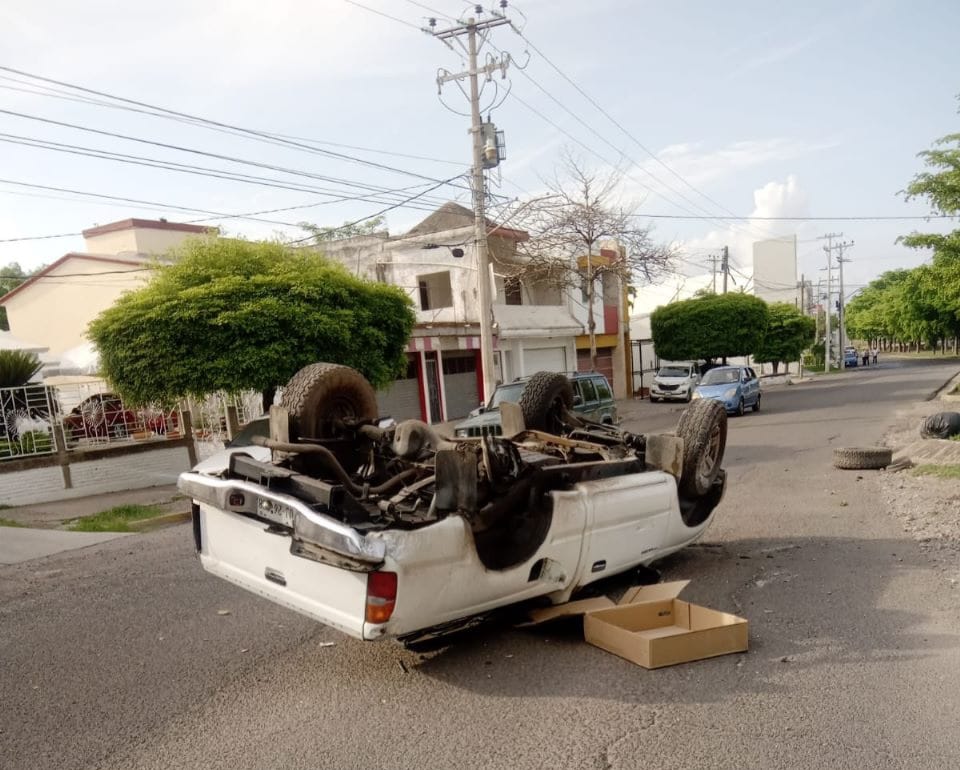 Camioneta con las llantas hacia arriba, casas, árboles, carros, postes y cables