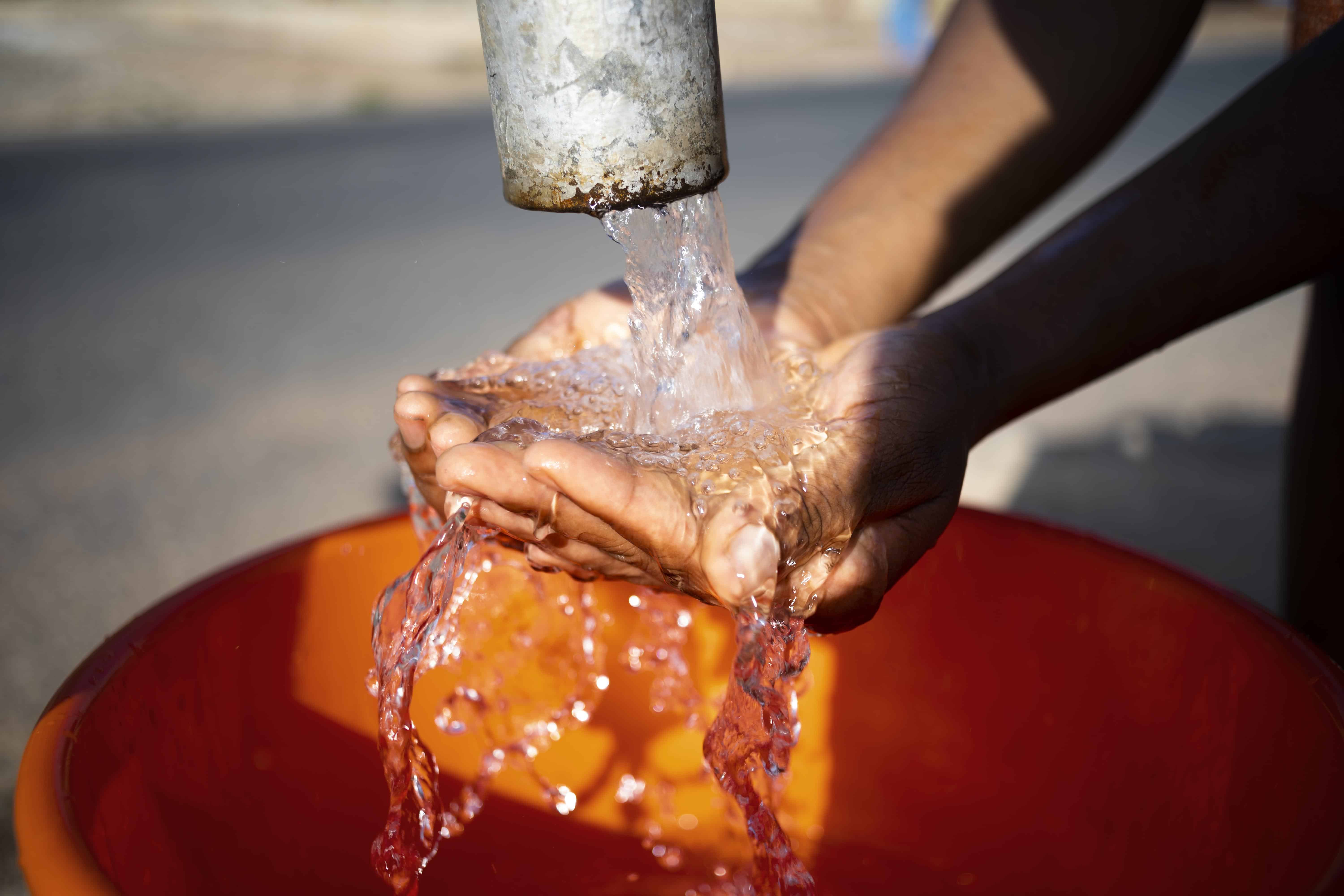 Manos de mujer bajo tubo de agua que cae a cubeta