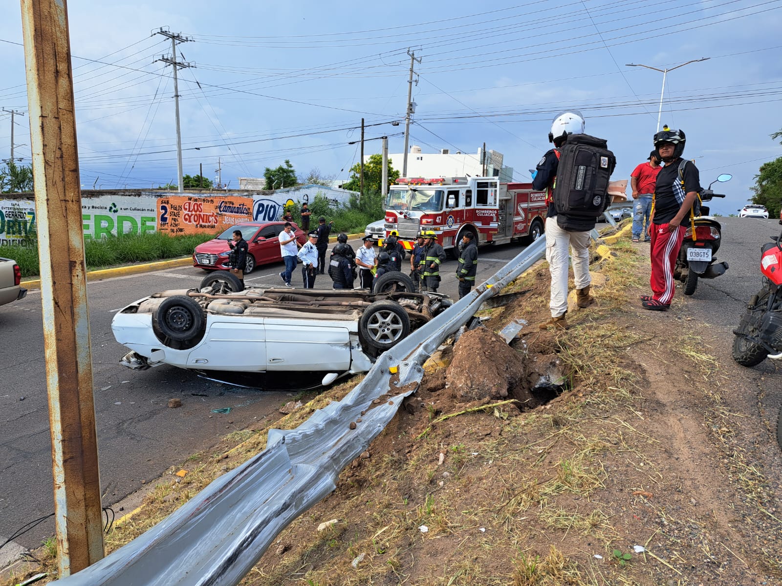 Vehículo color blanco volcado con las llantas hacia arriba. Hay presencia de paramédicos, policías y bomberos