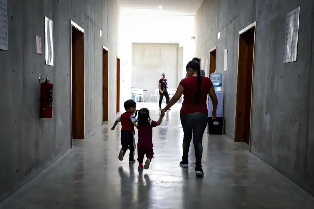 Familia migrante tomada de la mano al interior del Centro de Asistencia Social para Migrantes de DIF Sinaloa