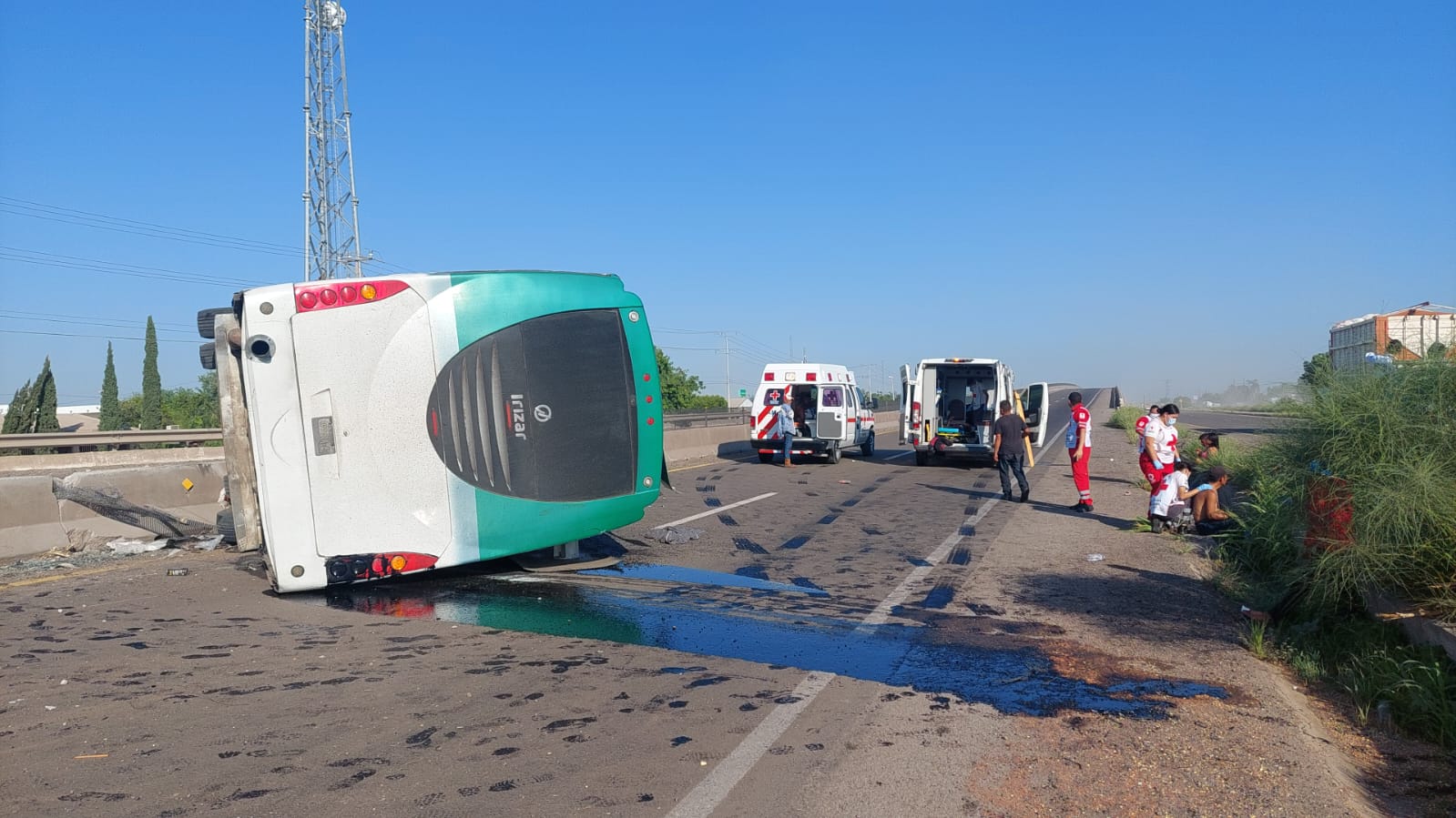 Un camión volcado sobre la carretera y al fondo 2 ambulancias y personas