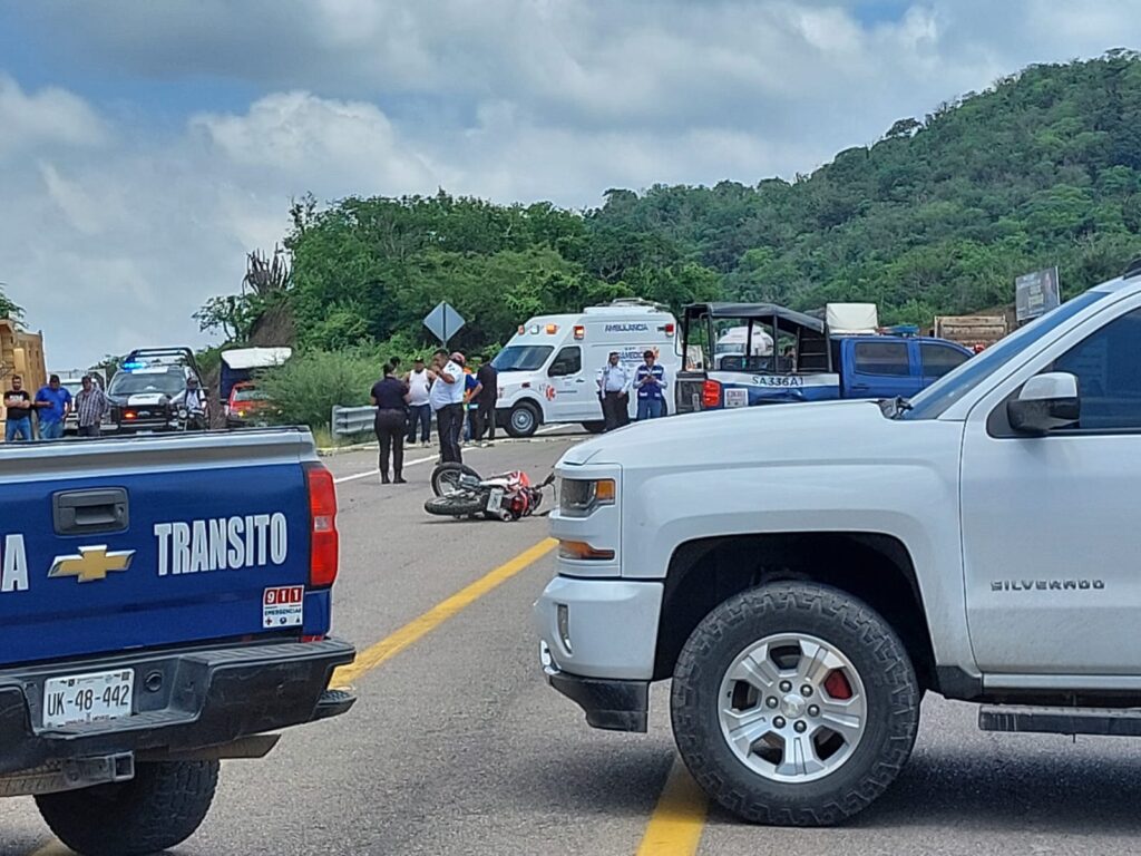 Personas sobre la carretera, una motocicleta y camionetas, al fondo árboles