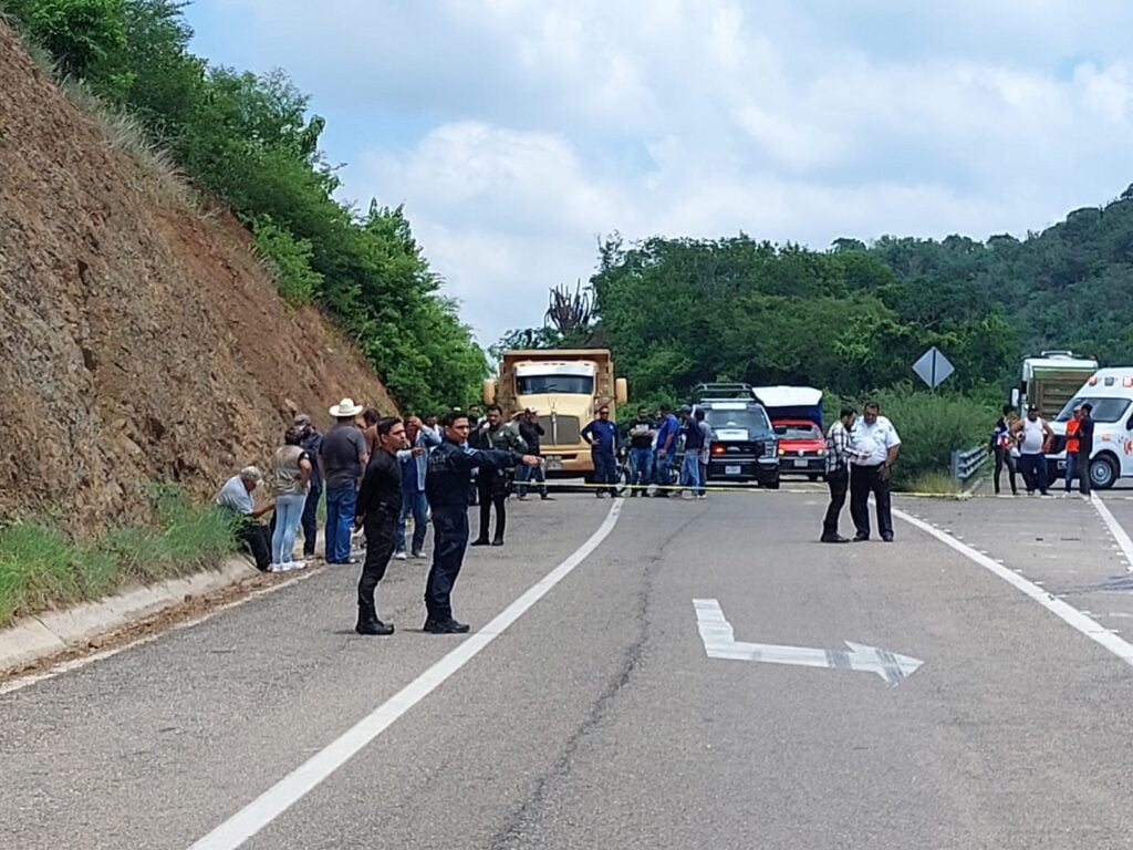 Personas sobre la carretera, un totón y camionetas, al fondo árboles