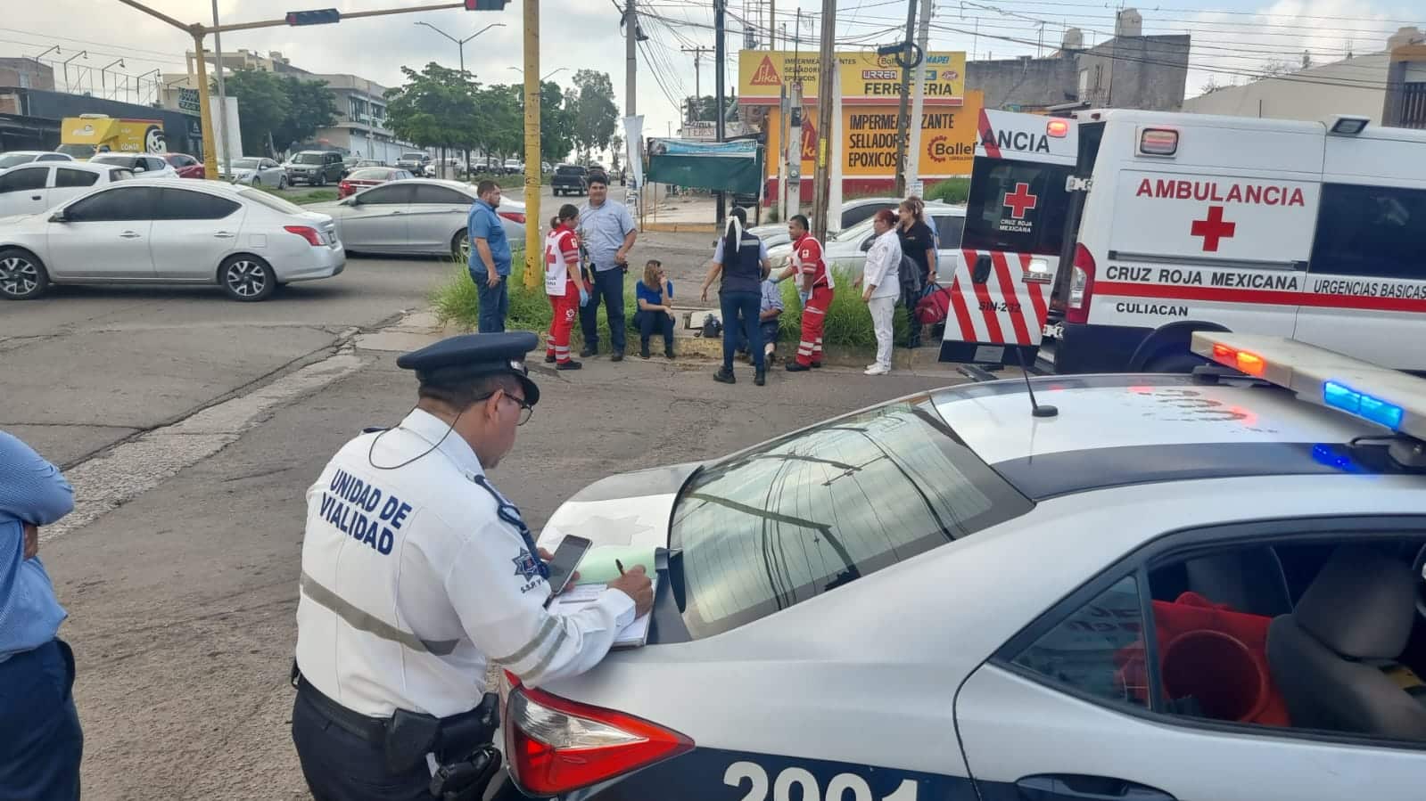 Carros, personas, un policía de tránsito, semáforos y una ambulancia de la Cruz Roja