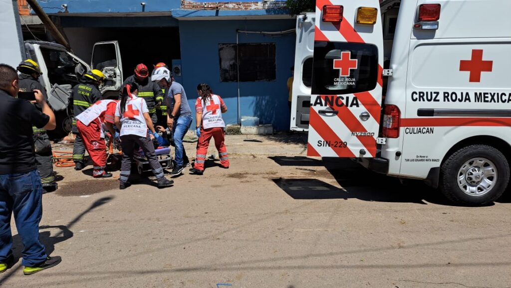Una ambulancia de Cruz Roja con las puertas traseras abiertas, un camión chocado y personas