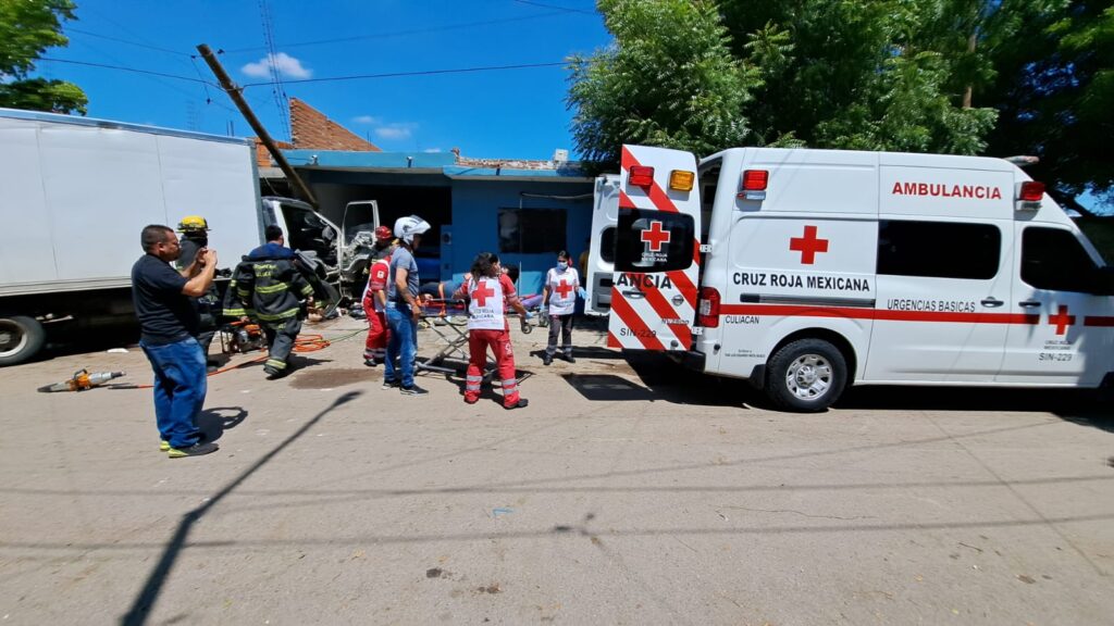 Una ambulancia de Cruz Roja con las puertas traseras abiertas, un camión chocado y personas