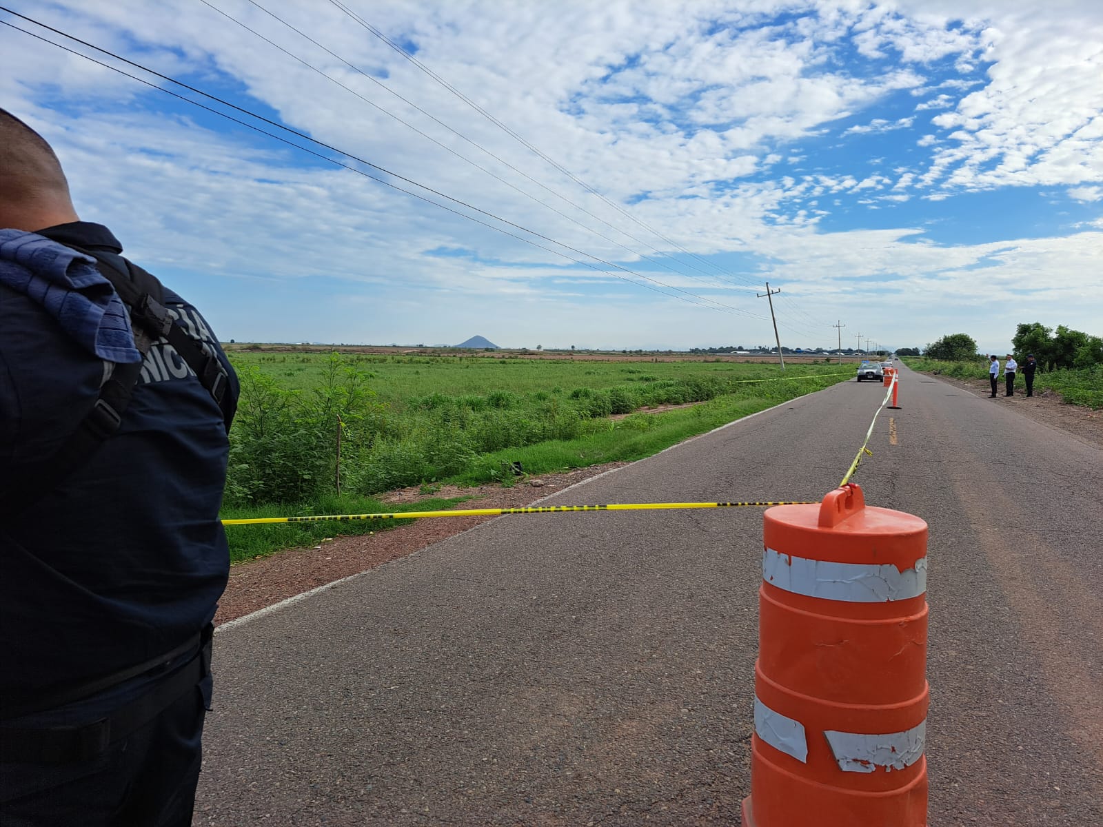 Cinta amarilla delimitando el área de un accidente, un cono anaranjado, una persona parada y una parcela verde