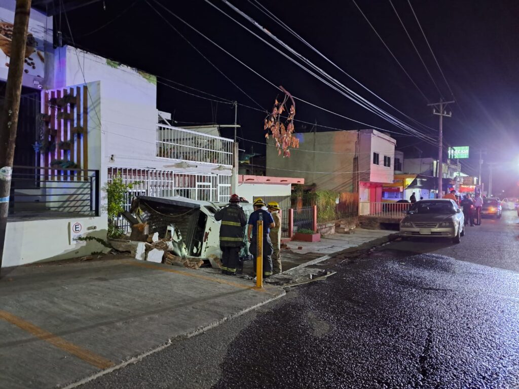 Personas mirando hacia una camioneta volcada sobre la banqueta, casas y carros estacionados