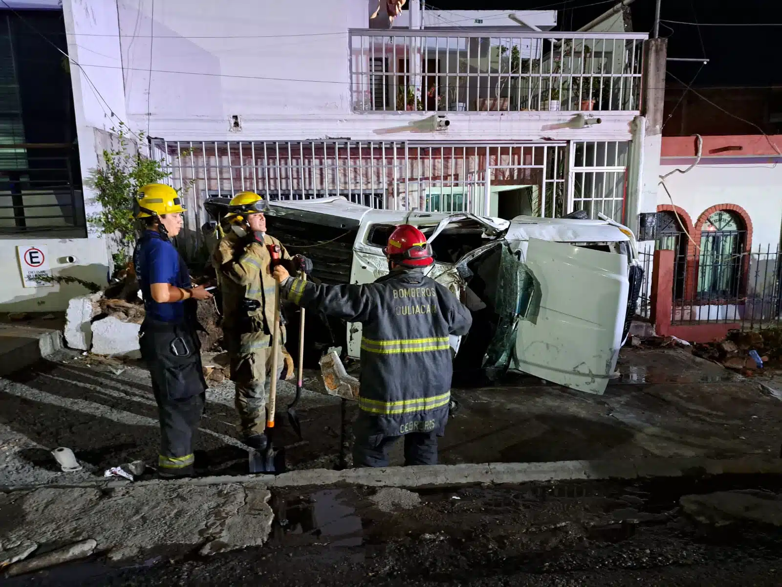 Personas mirando hacia una camioneta volcada sobre la banqueta, casas