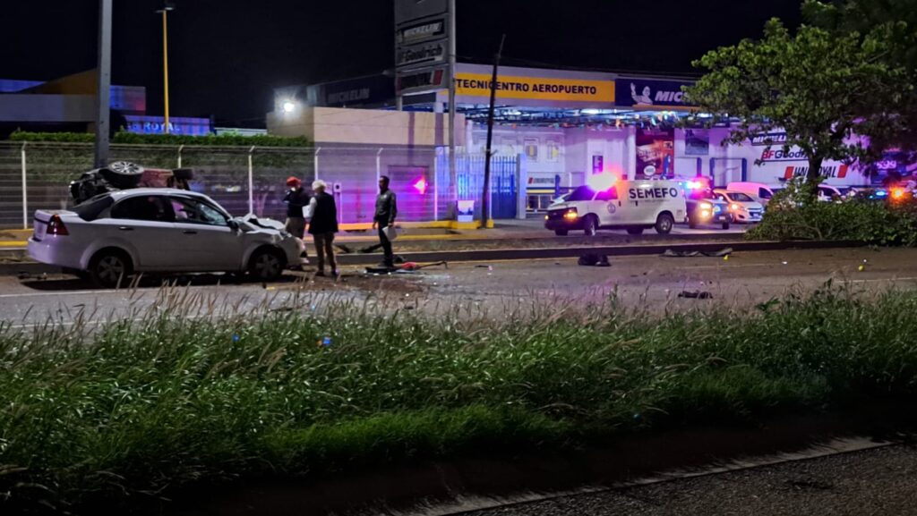 Un carro volcado y otro chocado del frente, camellón, árboles y personas