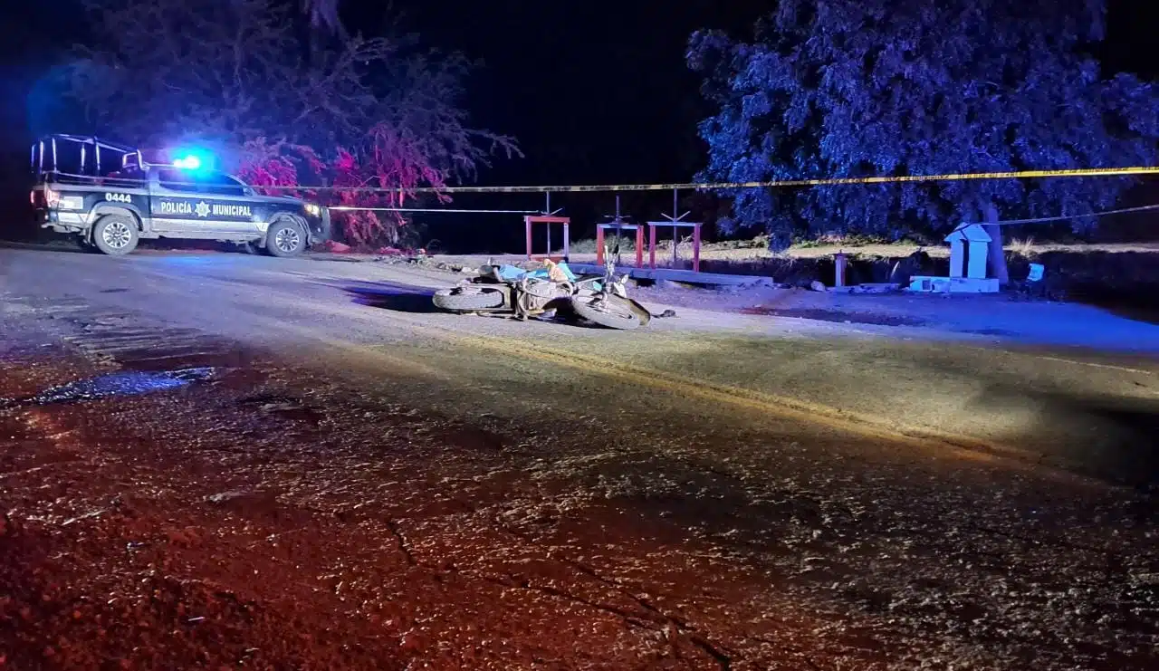 Moto tirada en la carretera en área demilitada con cinta amarilla y una patrulla al fondo tras asesinato de un motociclista